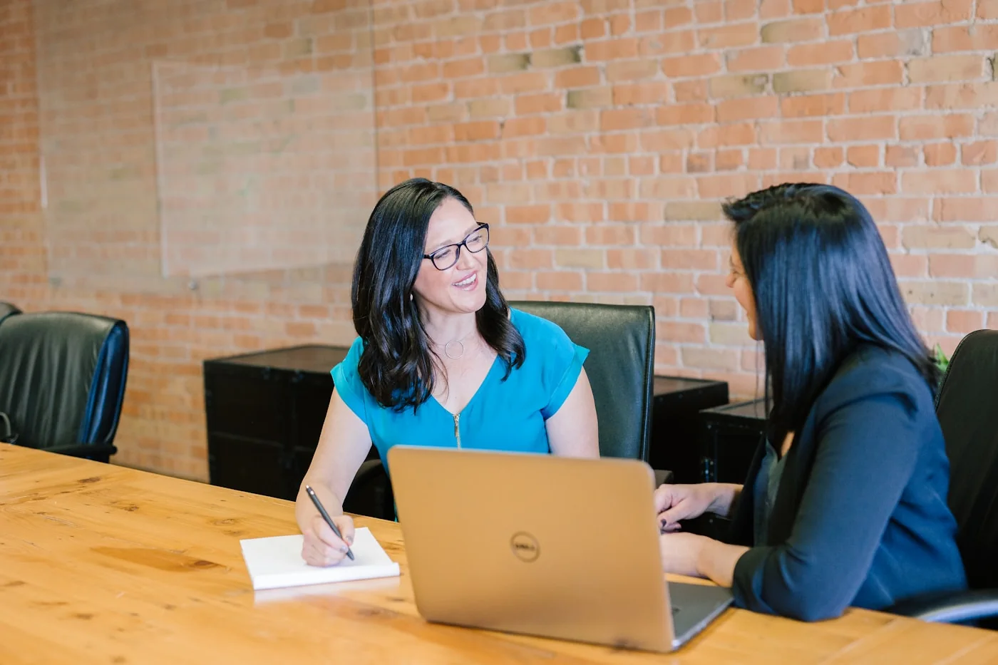 Two colleagues talking across a laptop in a meeting room