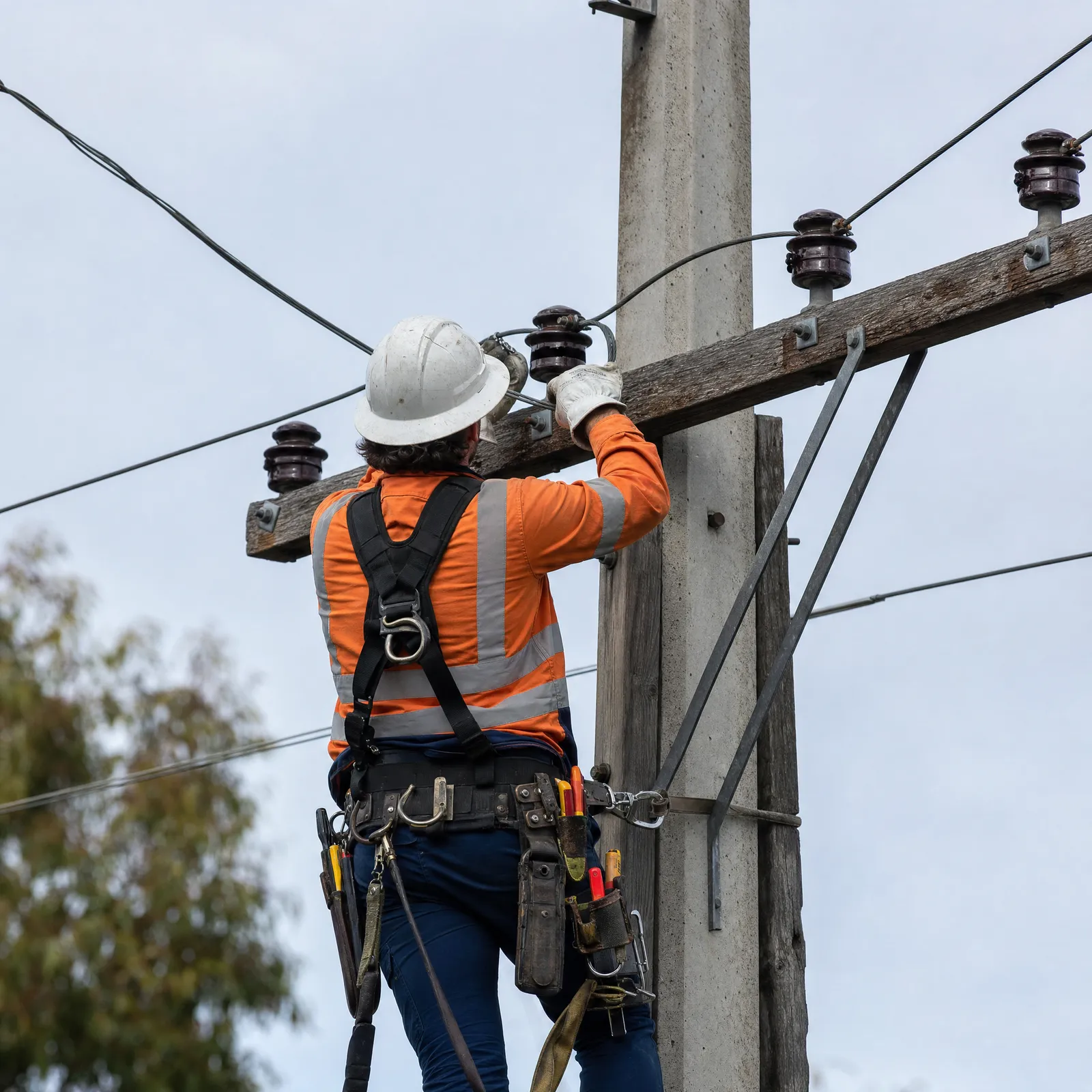 A lineworker in high-visibility gear working on power pole conductors